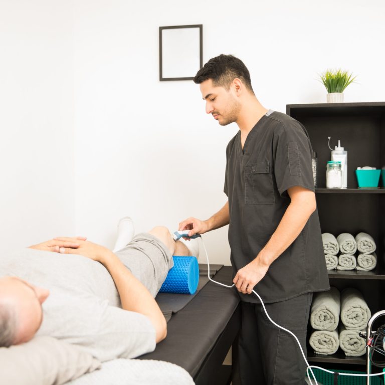 Physical therapist using ultrasound probe on patient knee while standing in hospital